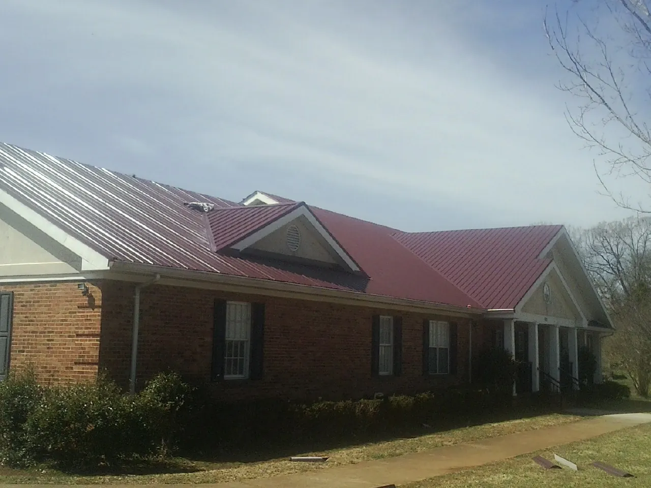 Red metal roof with gabled entries on a long brick building, from a Hail Damage Roof Repair job in Egypt