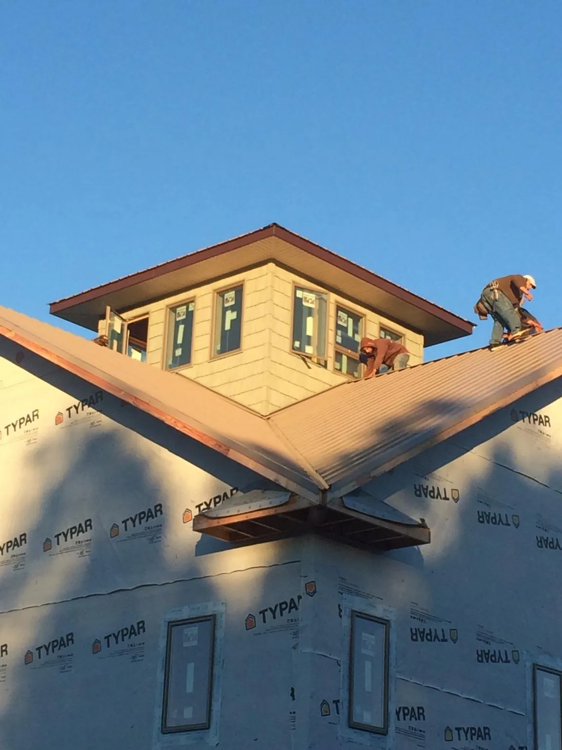 Roofers working around a rooftop cupola on a new metal roof at sunset — Roof Waterproofing in Egypt by Roofing Brothers